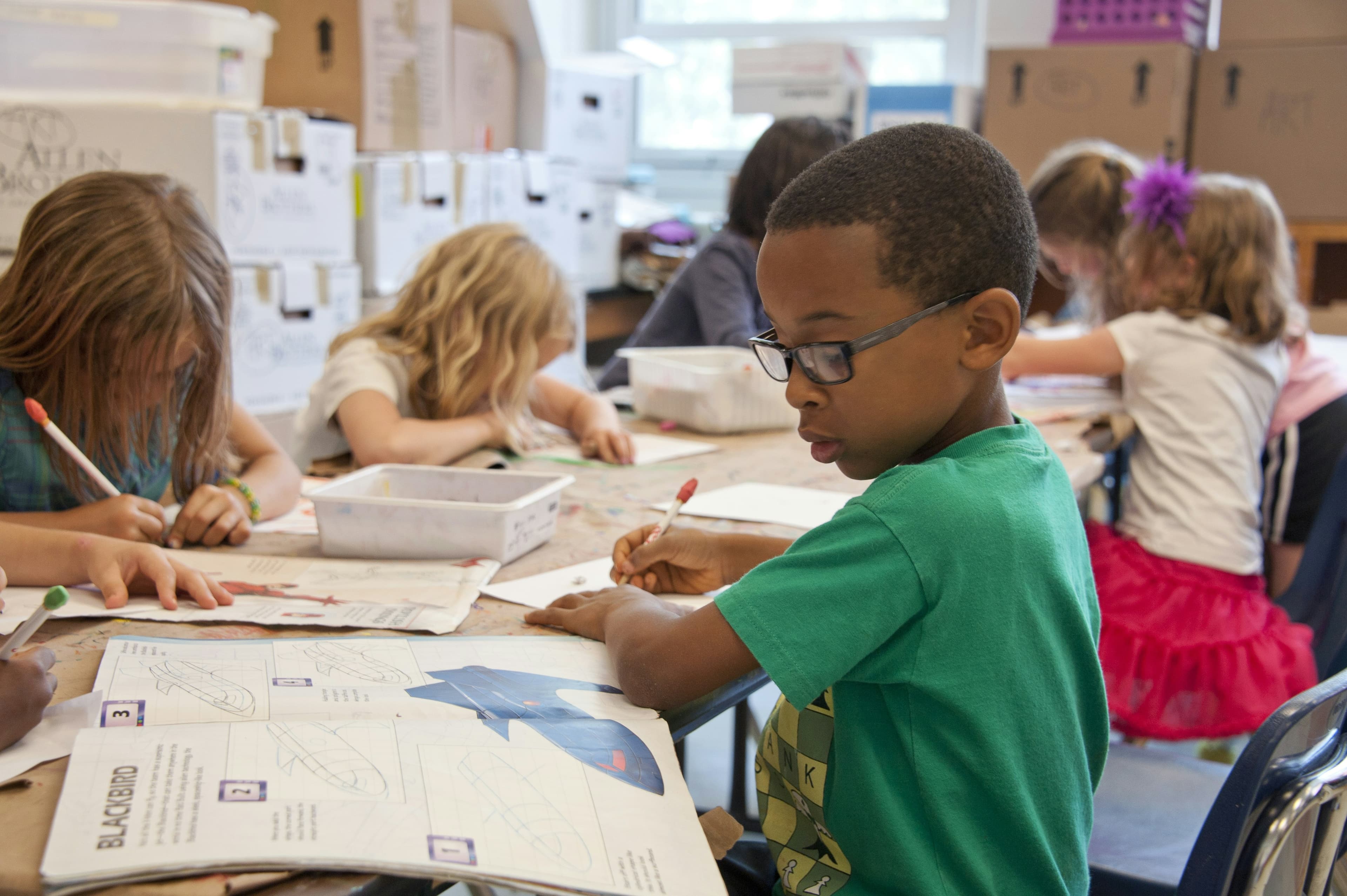 african american boy in elementary school, wearing green tee-shirt, drawing planes on white paper